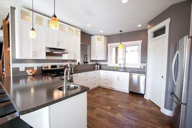 Inspiration for a mid-sized timeless u-shaped dark wood floor eat-in kitchen remodel in Vancouver with a drop-in sink, shaker cabinets, white cabinets, laminate countertops, gray backsplash, ceramic backsplash, stainless steel appliances and a peninsula