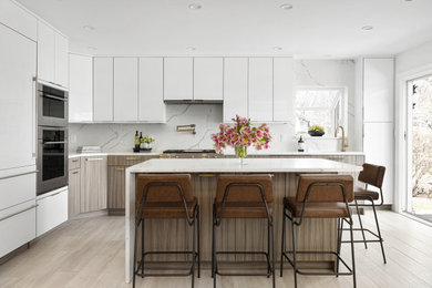 Example of a trendy l-shaped kitchen design in Boston with an undermount sink, flat-panel cabinets, white cabinets, quartz countertops, white backsplash, quartz backsplash, stainless steel appliances, an island and white countertops