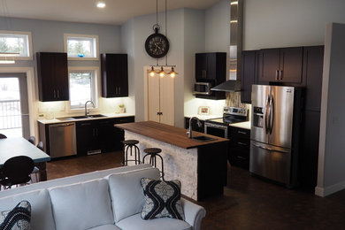 Large trendy l-shaped brown floor open concept kitchen photo in Other with a drop-in sink, solid surface countertops, multicolored backsplash, glass tile backsplash, shaker cabinets, stainless steel appliances and an island