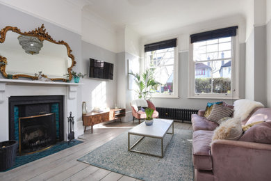ロンドンにある高級な中くらいなおしゃれなLDK (グレーの壁、塗装フローリング、標準型暖炉、漆喰の暖炉まわり、壁掛け型テレビ、グレーの床) の写真