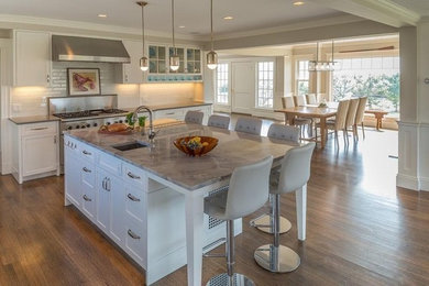 Example of a mid-sized beach style u-shaped medium tone wood floor and brown floor eat-in kitchen design in Boston with an undermount sink, recessed-panel cabinets, white cabinets, marble countertops, white backsplash, subway tile backsplash, stainless steel appliances, an island and gray countertops