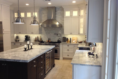 Large transitional u-shaped travertine floor and beige floor kitchen photo in Miami with a farmhouse sink, recessed-panel cabinets, white cabinets, marble countertops, stainless steel appliances, an island, white backsplash and stone tile backsplash
