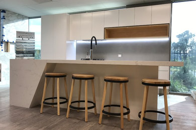 Inspiration for a mid-sized modern galley open plan kitchen in Melbourne with an undermount sink, flat-panel cabinets, white cabinets, quartz benchtops, grey splashback, porcelain splashback, black appliances, vinyl floors, with island and grey floor.