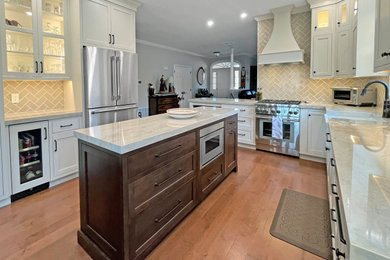 Inspiration for a mid-sized transitional l-shaped medium tone wood floor and brown floor kitchen remodel in Philadelphia with a farmhouse sink, beaded inset cabinets, beige cabinets, quartz countertops, beige backsplash, glass tile backsplash, paneled appliances, an island and brown countertops