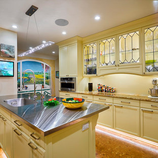 Mittelgroße Klassische Küche in U-Form mit Vorratsschrank, integriertem Waschbecken, Glasfronten, gelben Schränken, Edelstahl-Arbeitsplatte, Küchenrückwand in Gelb, Glasrückwand, Küchengeräten aus Edelstahl, Korkboden, Kücheninsel, braunem Boden und bunter Arbeitsplatte in Cleveland