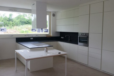 Inredning av ett modernt stort kök, med en undermonterad diskho, släta luckor, vita skåp, granitbänkskiva, svart stänkskydd, rostfria vitvaror och en köksö