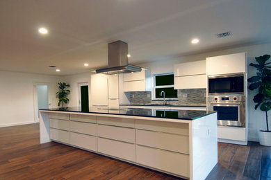 Huge minimalist single-wall porcelain tile and brown floor eat-in kitchen photo in Miami with a drop-in sink, white cabinets, granite countertops, multicolored backsplash, stainless steel appliances, an island and black countertops