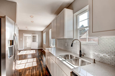 Eat-in kitchen - small modern galley dark wood floor and brown floor eat-in kitchen idea in Denver with a double-bowl sink, shaker cabinets, white cabinets, quartz countertops, white backsplash, glass sheet backsplash, stainless steel appliances and no island