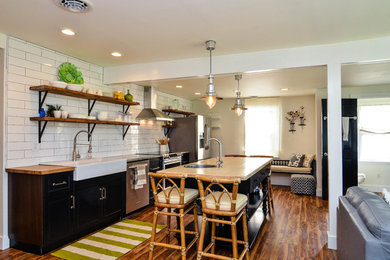 Inspiration for a mid-sized country medium tone wood floor open concept kitchen remodel in DC Metro with a farmhouse sink, recessed-panel cabinets, black cabinets, granite countertops, white backsplash, subway tile backsplash, stainless steel appliances and an island