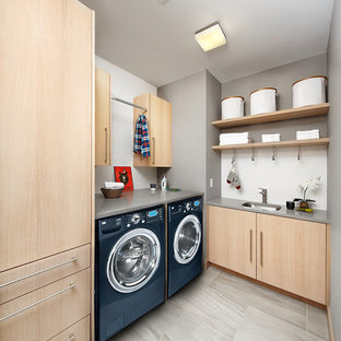 Foto de lavadero multiusos y en L, moderno, de tamaño medio, con fregadero bajoencimera, armarios con paneles lisos, puertas de armario de madera clara, encimera de cuarzo compacto, paredes grises, suelo de baldosas de porcelana y lavadora y secadora juntas