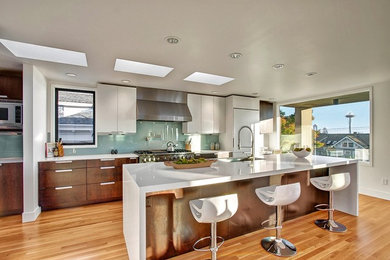 Example of a large minimalist single-wall medium tone wood floor eat-in kitchen design in Seattle with flat-panel cabinets, white cabinets, green backsplash, white appliances and an island