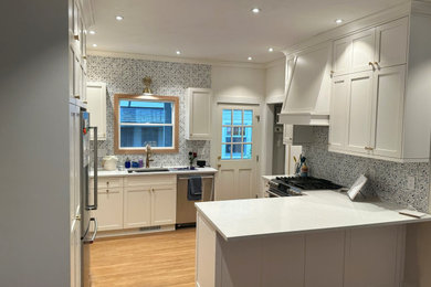 Medium sized traditional u-shaped enclosed kitchen in Seattle with shaker cabinets, white cabinets, engineered stone countertops, a breakfast bar, white worktops, stainless steel appliances and medium hardwood flooring.