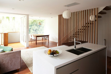 This is an example of a mid-sized contemporary galley open plan kitchen in Sydney with an undermount sink, flat-panel cabinets, green cabinets, solid surface benchtops, stainless steel appliances, medium hardwood floors and with island.