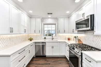 Mid-sized minimalist u-shaped vinyl floor and brown floor kitchen photo in DC Metro with an undermount sink, shaker cabinets, white cabinets, quartzite countertops, white backsplash, marble backsplash, stainless steel appliances, an island and white countertops
