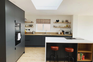 Photo of a large modern l-shaped open plan kitchen in Other with a double-bowl sink, flat-panel cabinets, grey cabinets, quartz worktops, black appliances, vinyl flooring, an island, brown floors, white worktops and feature lighting.