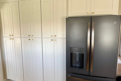Inspiration for a mid-sized u-shaped vinyl floor and brown floor enclosed kitchen remodel in Other with shaker cabinets, white cabinets, quartz countertops, white countertops, white backsplash, ceramic backsplash, black appliances and a farmhouse sink