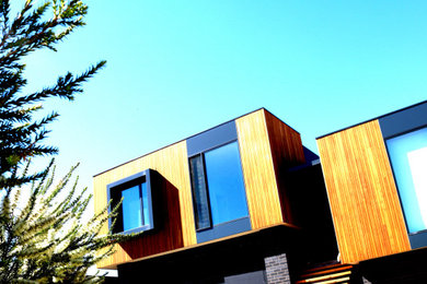 This is an example of a mid-sized beach style two-storey house exterior in Geelong with wood siding, a flat roof and a metal roof.