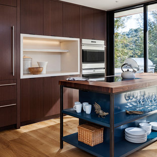 Foto de cocina actual con armarios con paneles lisos, puertas de armario de madera en tonos medios, encimera de madera, electrodomésticos de acero inoxidable, suelo de madera clara, una isla y suelo beige