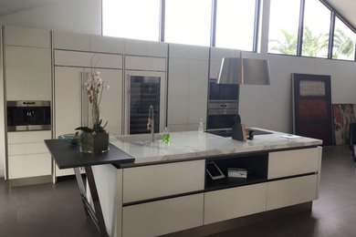 Mid-sized trendy galley porcelain tile and brown floor kitchen pantry photo in Miami with white cabinets, stainless steel appliances, an island, an undermount sink, flat-panel cabinets and marble countertops