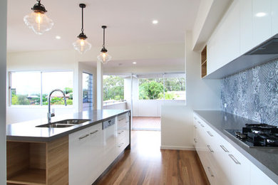Design ideas for a small midcentury galley open plan kitchen in Brisbane with a double-bowl sink, flat-panel cabinets, white cabinets, quartz benchtops, blue splashback, porcelain splashback, black appliances, dark hardwood floors, with island and brown floor.