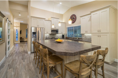 Inspiration for a mid-sized transitional l-shaped open plan kitchen in Phoenix with shaker cabinets, white cabinets, stainless steel appliances, with island, an undermount sink, granite benchtops, grey splashback, stone tile splashback, brown floor, brown benchtop and laminate floors.