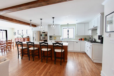 Open concept kitchen - huge country l-shaped medium tone wood floor and brown floor open concept kitchen idea in New York with an undermount sink, shaker cabinets, white cabinets, quartz countertops, beige backsplash, ceramic backsplash, stainless steel appliances, an island and white countertops