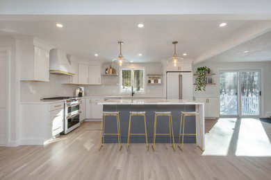 This is an example of a mid-sized modern l-shaped eat-in kitchen in Boston with an undermount sink, shaker cabinets, white cabinets, quartz benchtops, white splashback, ceramic splashback, white appliances, light hardwood floors, with island, white floor and white benchtop.