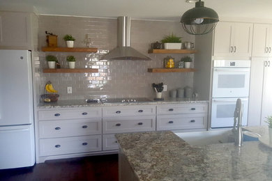 Kitchen - large farmhouse dark wood floor and brown floor kitchen idea in Dallas with a farmhouse sink, shaker cabinets, beige cabinets, granite countertops, beige backsplash, subway tile backsplash, white appliances, an island and multicolored countertops
