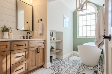 This is an example of a mid-sized country master bathroom in Baltimore with shaker cabinets, light wood cabinets, a freestanding tub, an alcove shower, white tile, porcelain tile, green walls, porcelain floors, an undermount sink, engineered quartz benchtops, black floor, a hinged shower door, white benchtops, a niche, a double vanity, a built-in vanity and vaulted.