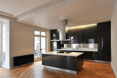 Réalisation d'une grande cuisine ouverte parallèle design avec un évier encastré, des portes de placard noires, un plan de travail en surface solide, une crédence métallisée, une crédence en dalle métallique, un électroménager en acier inoxydable, parquet clair, îlot, un sol beige et un plan de travail blanc.