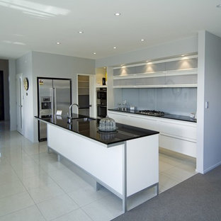 Mittelgroße Moderne Küche in L-Form mit Küchenrückwand in Grau, Glasrückwand, Kücheninsel, Vorratsschrank, Waschbecken, flächenbündigen Schrankfronten, weißen Schränken, Granit-Arbeitsplatte, Küchengeräten aus Edelstahl und Keramikboden in Christchurch