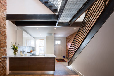 Example of a mid-sized minimalist l-shaped light wood floor open concept kitchen design in New York with an undermount sink, flat-panel cabinets, white cabinets, quartzite countertops, white backsplash, stone slab backsplash, stainless steel appliances and a peninsula