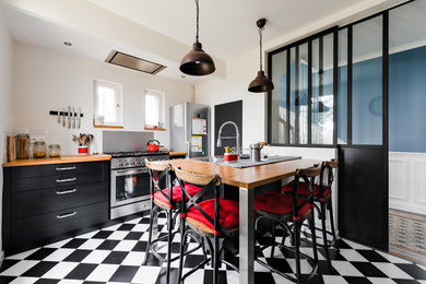 Photo of a mid-sized industrial galley separate kitchen in Paris with a double-bowl sink, shaker cabinets, black cabinets, wood benchtops, white splashback, subway tile splashback, stainless steel appliances, a peninsula, ceramic floors, black floor and brown benchtop.