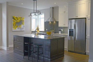 Inspiration for a mid-sized transitional single-wall medium tone wood floor eat-in kitchen remodel in Orange County with a farmhouse sink, shaker cabinets, white cabinets, granite countertops, gray backsplash, glass tile backsplash, stainless steel appliances and an island