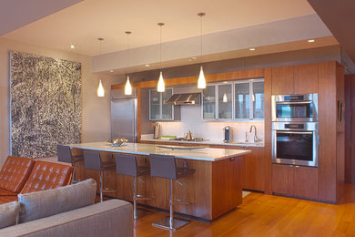 Example of a mid-sized minimalist galley medium tone wood floor open concept kitchen design in Boston with an undermount sink, flat-panel cabinets, medium tone wood cabinets, quartz countertops, white backsplash, glass sheet backsplash, stainless steel appliances and an island