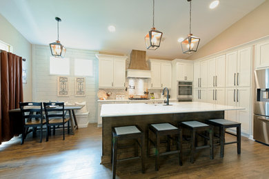 Example of a cottage laminate floor and brown floor kitchen design in Other with a farmhouse sink, white cabinets, quartz countertops, white backsplash, stainless steel appliances, an island and white countertops