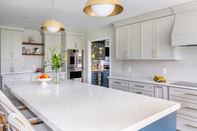 Example of a large transitional medium tone wood floor and brown floor kitchen pantry design in Baltimore with a farmhouse sink, shaker cabinets, white cabinets, quartz countertops, beige backsplash, ceramic backsplash, stainless steel appliances and an island