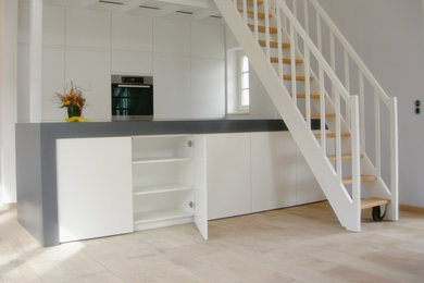 Offene Moderne Küche mit Einbauwaschbecken, flächenbündigen Schrankfronten, weißen Schränken, Arbeitsplatte aus Holz, Küchenrückwand in Weiß, Küchengeräten aus Edelstahl, hellem Holzboden und Halbinsel in Köln