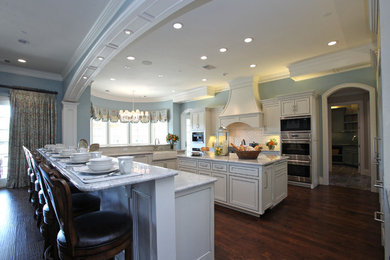 Example of a large classic l-shaped dark wood floor and brown floor eat-in kitchen design in Dallas with a farmhouse sink, shaker cabinets, white cabinets, granite countertops, white backsplash, subway tile backsplash, paneled appliances and two islands