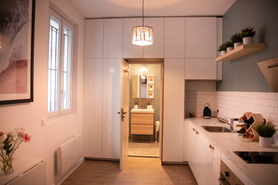 Idée de décoration pour une cuisine ouverte nordique en L de taille moyenne avec un évier 1 bac, un placard à porte affleurante, des portes de placard blanches, un plan de travail en stratifié, une crédence blanche, une crédence en carrelage métro, un électroménager en acier inoxydable, parquet clair, aucun îlot, un sol beige et un plan de travail blanc.