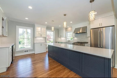 Inspiration for a large transitional single-wall medium tone wood floor and brown floor eat-in kitchen remodel in New York with an undermount sink, shaker cabinets, white cabinets, quartz countertops, white backsplash, stainless steel appliances, an island and white countertops