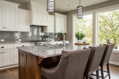 Inspiration for a mid-sized transitional medium tone wood floor eat-in kitchen remodel in Atlanta with an undermount sink, shaker cabinets, white cabinets, granite countertops, gray backsplash, glass tile backsplash, stainless steel appliances and an island