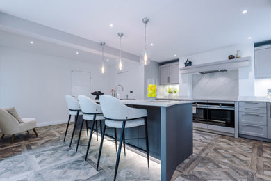 Inspiration for a large contemporary open plan kitchen in Manchester with a built-in sink, shaker cabinets, engineered quartz splashback, stainless steel appliances and white worktops.