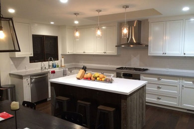 Inspiration for a mid-sized transitional u-shaped dark wood floor eat-in kitchen remodel in San Francisco with a farmhouse sink, beaded inset cabinets, white cabinets, solid surface countertops, white backsplash, stone tile backsplash, stainless steel appliances and an island