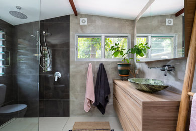 This is an example of a contemporary bathroom in Sunshine Coast with flat-panel cabinets, medium wood cabinets, a curbless shower, gray tile, a vessel sink, wood benchtops, beige floor, an open shower, brown benchtops, a single vanity, a floating vanity and vaulted.