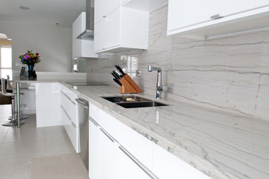 Open concept kitchen - large contemporary galley porcelain tile and beige floor open concept kitchen idea in Toronto with a double-bowl sink, flat-panel cabinets, white cabinets, quartzite countertops, gray backsplash, stone slab backsplash, stainless steel appliances, no island and white countertops