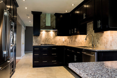 Small transitional l-shaped limestone floor enclosed kitchen photo in Toronto with beige backsplash, stone slab backsplash, stainless steel appliances, an island, an undermount sink, shaker cabinets, black cabinets and granite countertops