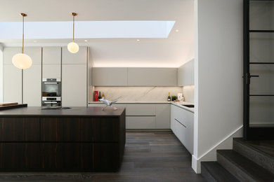 Photo of a mid-sized contemporary l-shaped kitchen in London with an undermount sink, grey cabinets, white splashback, marble splashback, stainless steel appliances, dark hardwood floors, with island, brown floor and white benchtop.