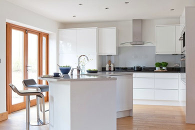 Design ideas for a mid-sized contemporary l-shaped eat-in kitchen in Kent with an undermount sink, flat-panel cabinets, white cabinets, quartzite benchtops, grey splashback, glass sheet splashback, stainless steel appliances, light hardwood floors and with island.