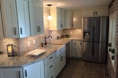 Photo of a small transitional l-shaped kitchen in Boston with a farmhouse sink, shaker cabinets, white cabinets, granite benchtops, beige splashback, stone tile splashback, stainless steel appliances, medium hardwood floors and no island.